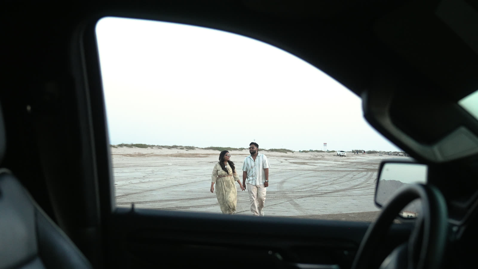 Vibha and Jishnu walking on the beach, seen through a car window